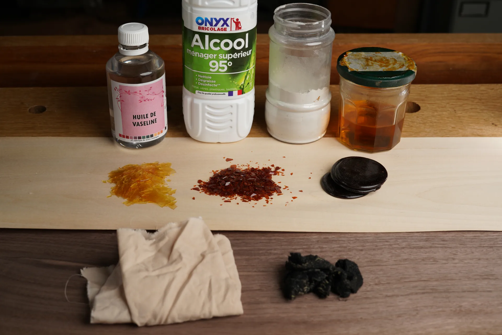 Shellac varieties laid out on a strip of light wood — dewaxed blond shellac and arathoune — alongside cotton cloth, wool, mineral oil, alcohol, pumice powder and prepared varnish